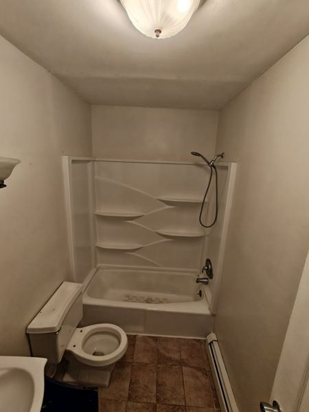 Bathroom before remodel: dated tub surround and tile floor